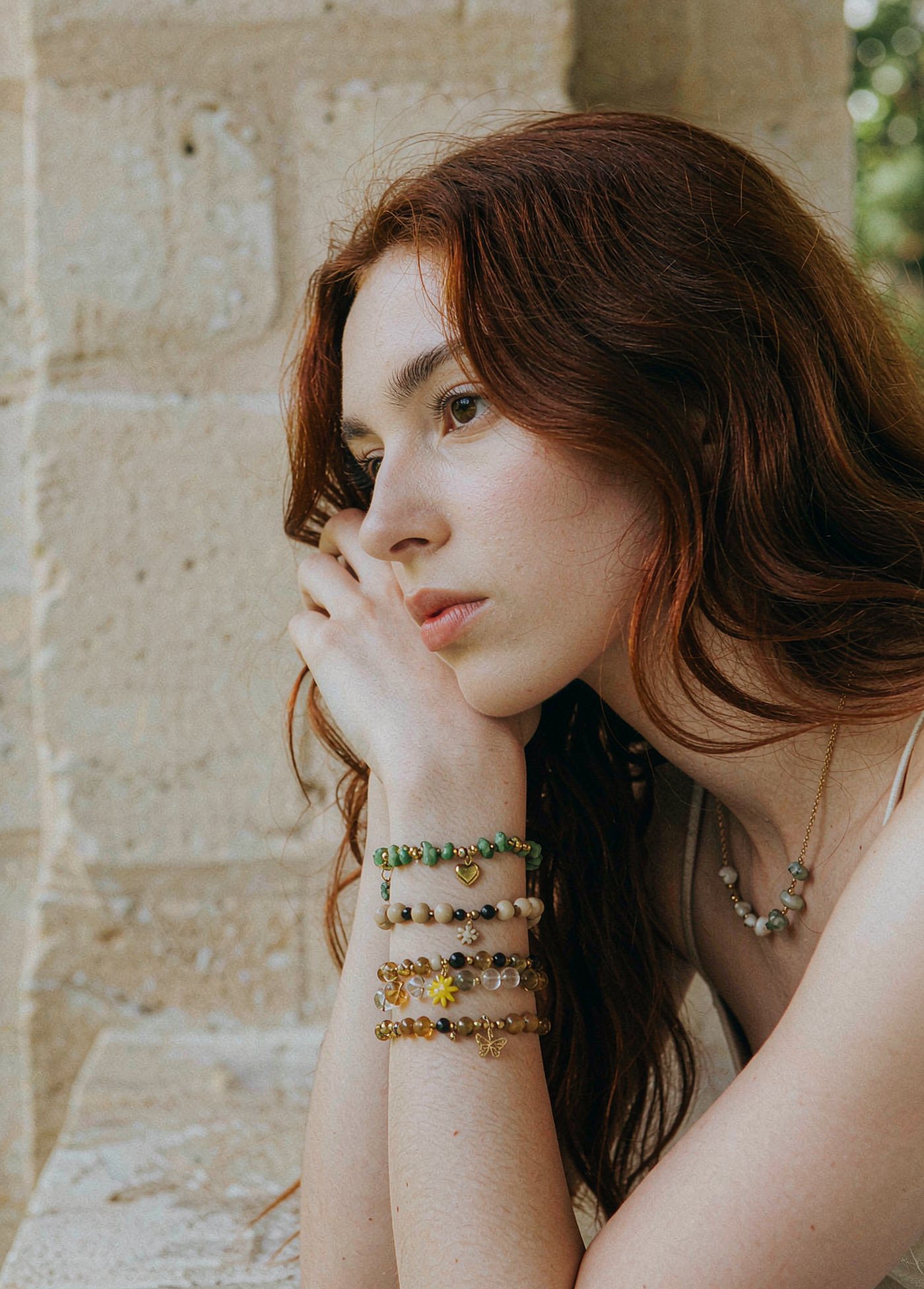 Model wearing stacked handmade beaded charm bracelets in warm earthy light
